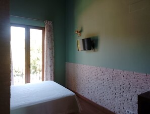 A room with a bed, a window with curtains, a wall-mounted TV, and a brick-patterned wall.