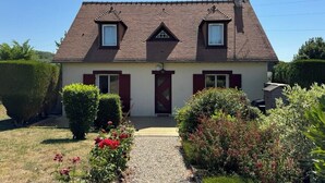 Ein zweigeschossiges Haus mit geneigtem Dach, einem Hauseingang und einem kleinen Garten mit Blumen und Sträuchern.