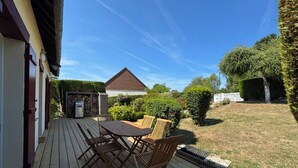 Eine Holzterrasse mit Tisch und Stühlen, ein kleines Gebäude und ein gepflegter Rasen.