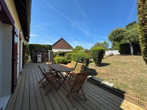 A wooden deck with a table and chairs, a small building, and a well-maintained lawn. - Quiet house with garden, 5 min from Deauville (Touques)