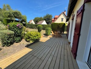 Um deck de madeira com área de estar e um jardim com diversas plantas e um arbusto.