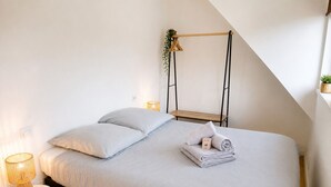 A neatly made bed with pillows, a bedside lamp, and a small table with a lamp. - A Cozy Nest Under the Roof (Wiwersheim)