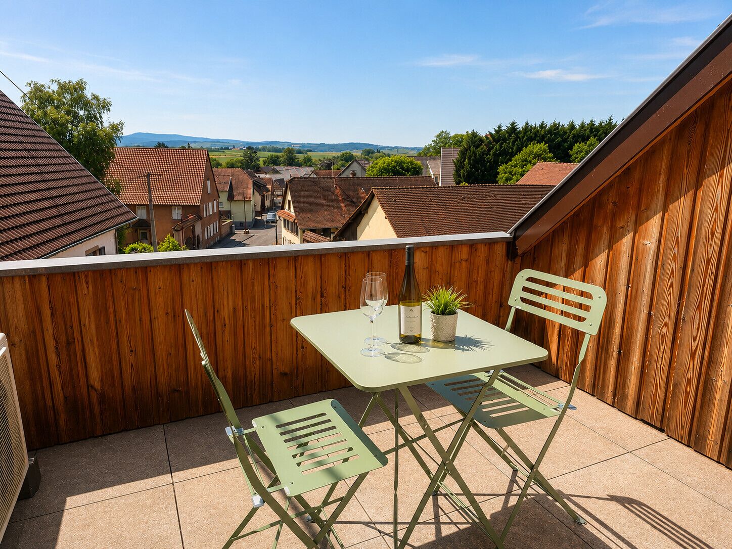 Un balcon avec une table et des chaises, une bouteille de vin et une petite plante.