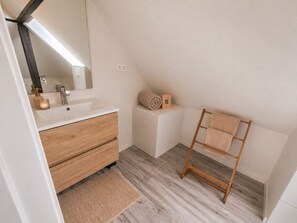 Ein modernes Badezimmer mit einem Holzwaschtisch, einem großen Spiegel und einem Handtuchhalter.