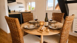 A dining area with a round table set for four, surrounded by wicker chairs with cushions. There is a bottle of wine and glasses on the table. - A Cozy Nest Under the Roof (Wiwersheim)