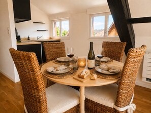 A dining area with a round table set for four, surrounded by wicker chairs with cushions. There is a bottle of wine and glasses on the table. - A Cozy Nest Under the Roof (Wiwersheim)