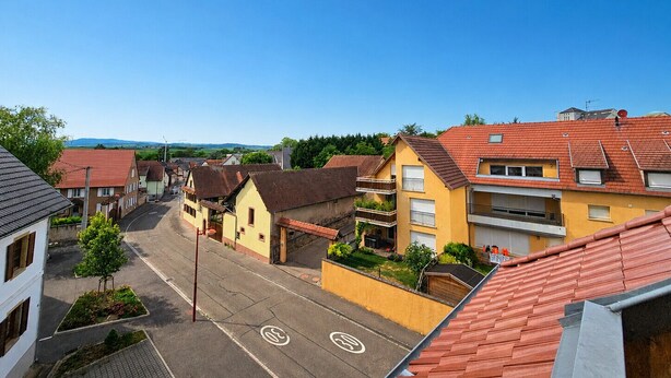 A residential street with houses, a clear sky, and a distant mountain range. - A Cozy Nest Under the Roof (Wiwersheim)
