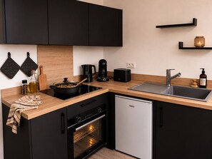 A modern kitchen with black cabinets, a stainless steel sink, a coffee maker, a toaster, and a dishwasher. - A Cozy Nest Under the Roof (Wiwersheim)