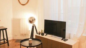 En stue med fjernsyn, et lille bord, en lampe og et spejl på væggen.
