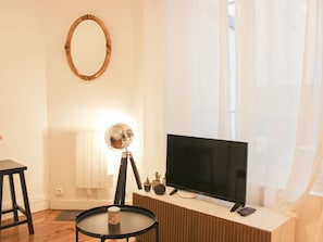 Ein Wohnzimmer mit Fernseher, einem kleinen Tisch, einer Lampe und einem Spiegel an der Wand.