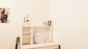 Et lille, hvidt skrivebord med en guitar, en lampe, en plante og bøger.