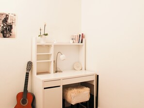 Ein kleiner, weißer Schreibtisch mit Gitarre, Lampe, Pflanze und Büchern.