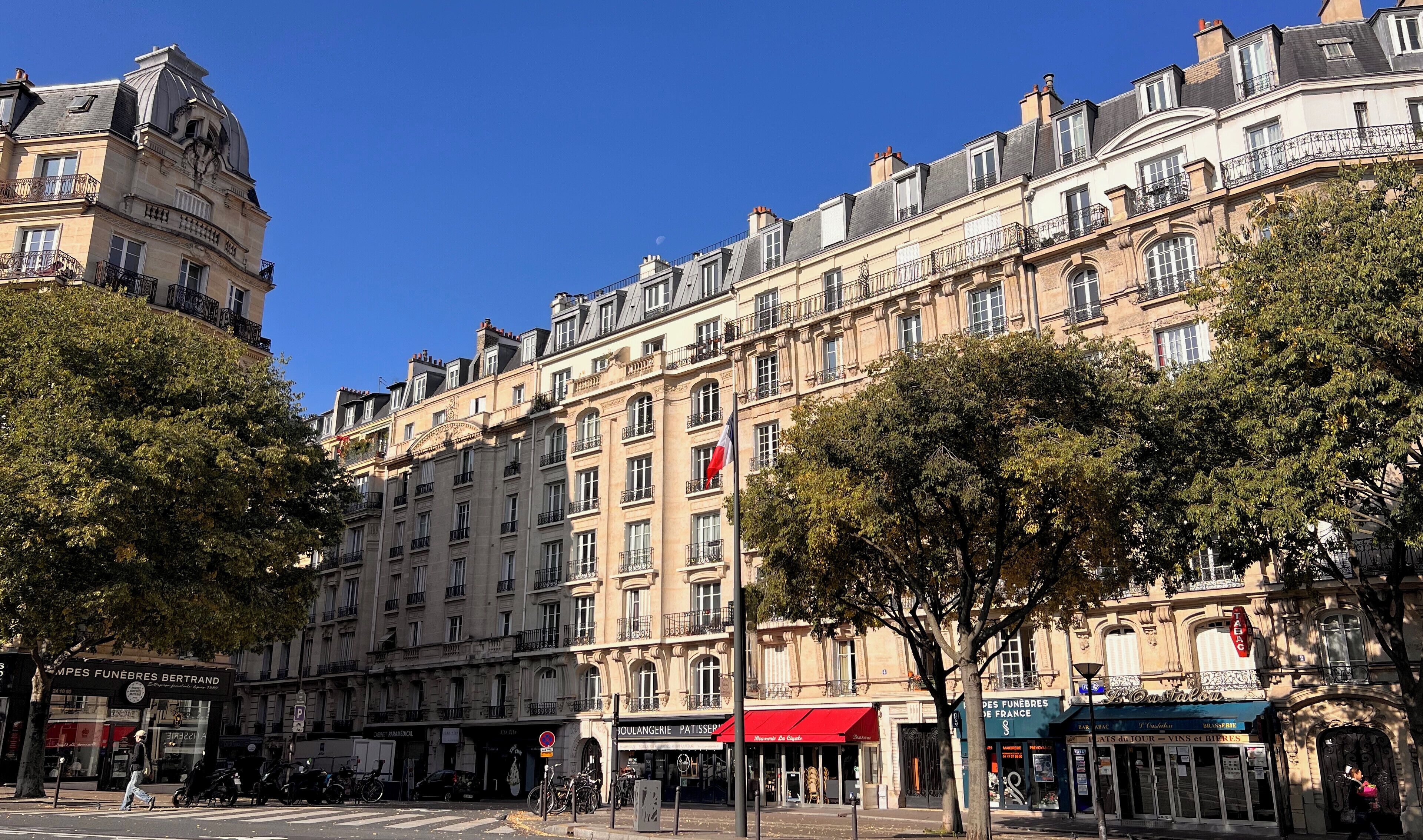 A multi-story building with a classic architectural style, featuring balconies and a flag.