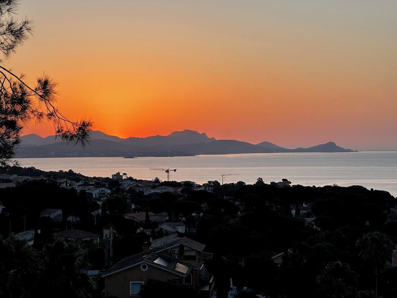 A coastal town at sunset with visible buildings, a crane, and distant mountains.