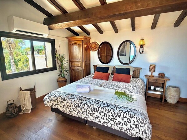 Une chambre à coucher avec un lit, une fenêtre, une armoire en bois, un miroir et une table de chevet.