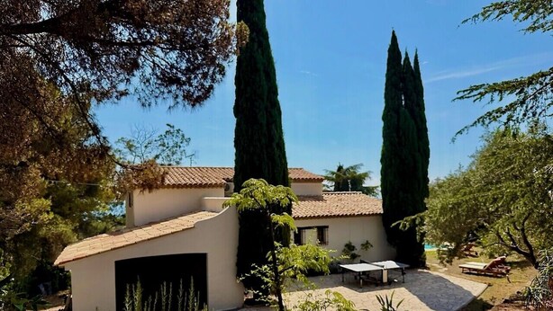 A house with a garage, a patio with a table and chairs, and tall cypress trees. - Villa with sea view and swimming pool in St-Aygulf (Fréjus)