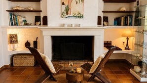 A living room with a fireplace, two armchairs, a coffee table, and shelves with books and decorative items. - Villa with sea view and swimming pool in St-Aygulf (Fréjus)