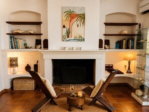 Ein Wohnzimmer mit Kamin, zwei Sesseln, einem Couchtisch und Regalen mit Büchern und Dekoration.