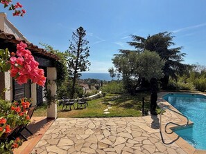 Un espace piscine agrémenté d’une terrasse en pierre, de mobilier d’extérieur et offrant une vue sur la mer.