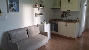 A living room with a sofa, a small white fridge, a coffee maker, and a kitchen with cabinets and a stove. - 38 Stay - One Bedroom Apartment, Sleeps 2 (Naples)