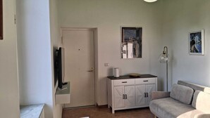Ein Zimmer mit einem weißen Schrank, einem Fernseher, einem gerahmten Kunstwerk und einem Sofa.