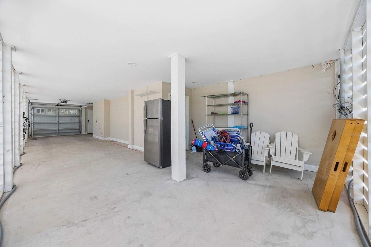 Un ampio garage con un frigorifero capiente, un carrello con vestiti piegati e un pannello di legno appoggiato al muro.
