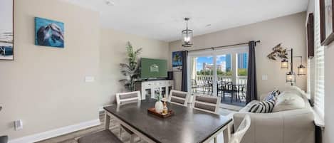 A dining area with a wooden table and chairs, a sofa, and a TV in the background.