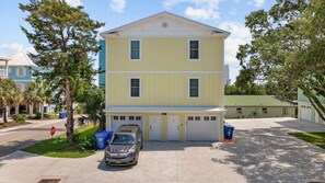 A two-story building with a garage, parked cars, and a stop sign. - Sunshine Derby-1 Block to Beach-garage EV Charger (Myrtle Beach)