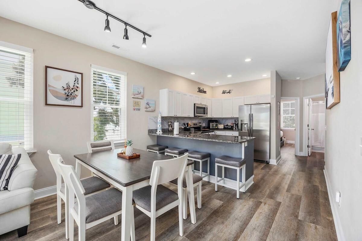 A modern kitchen with white cabinets, a central island, and a dining area with a table and chairs.
