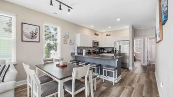 A modern kitchen with white cabinets, a central island, and a dining area with a table and chairs.