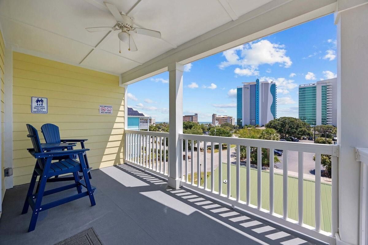 A balcony with a white railing, a ceiling fan, and a view of city buildings.