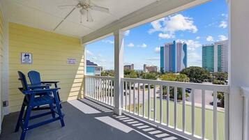 A balcony with a white railing, a ceiling fan, and a view of city buildings.