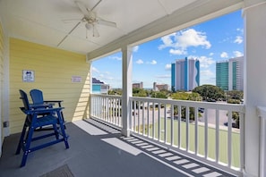 A balcony with a white railing, a ceiling fan, and a view of city buildings. - Sunshine Derby-1 Block to Beach-garage EV Charger (Myrtle Beach)