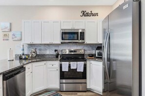 A modern kitchen with white cabinets, stainless steel appliances, and a marble countertop. - Sunshine Derby-1 Block to Beach-garage EV Charger (Myrtle Beach)