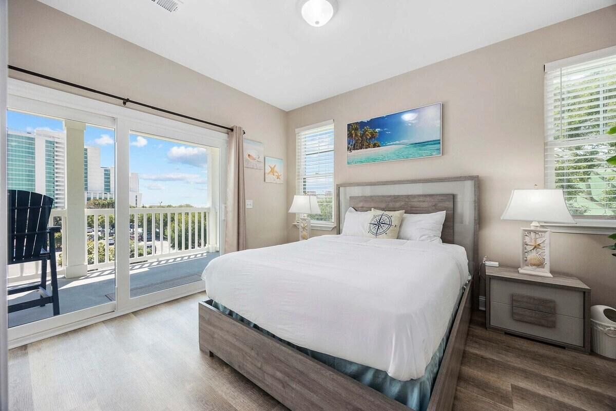 Ein Schlafzimmer mit einem großen Bett, einem Nachttisch, einem Sessel und einem Balkon mit Blick auf Gebäude.