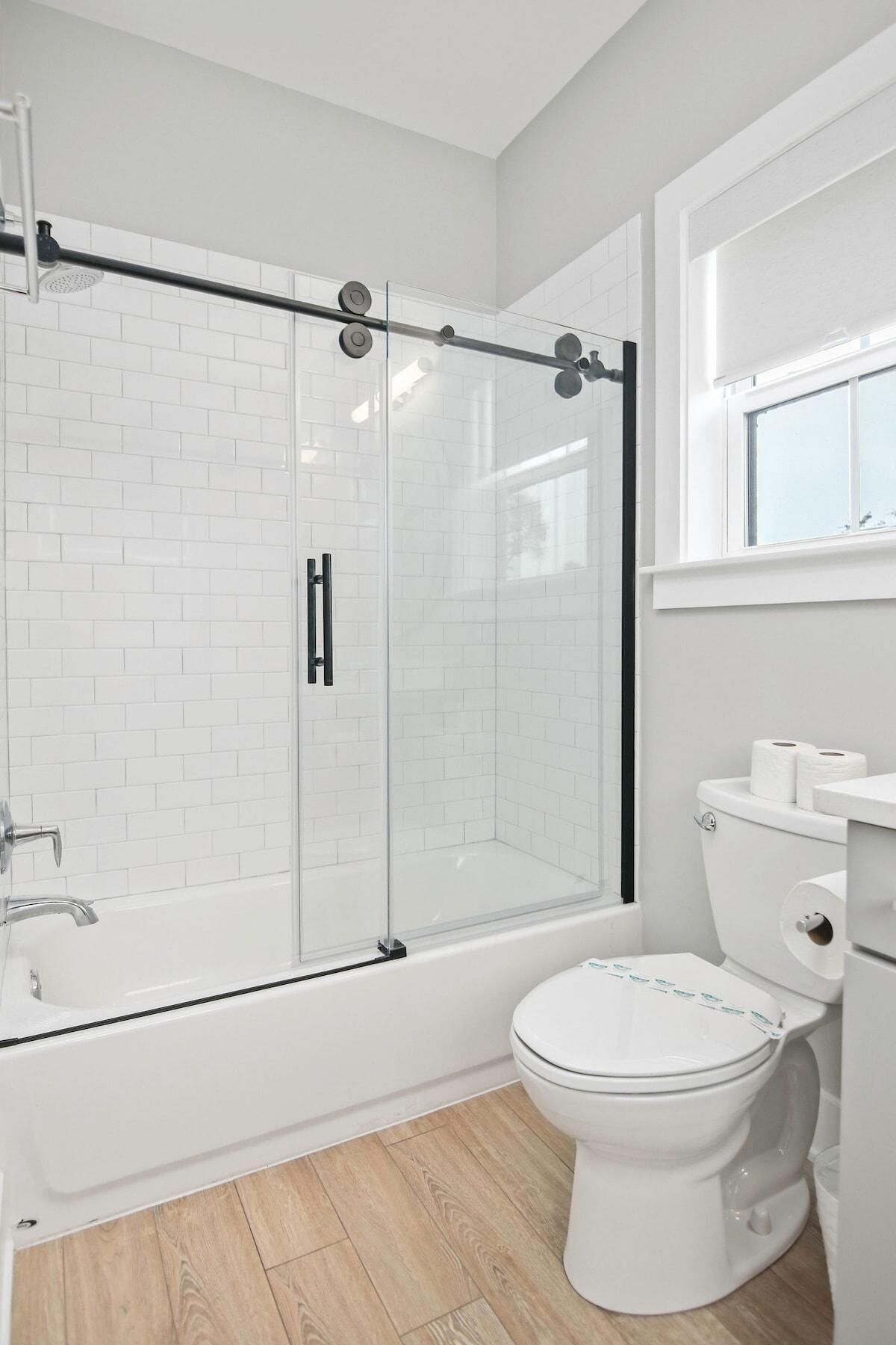 A modern bathroom with a glass-enclosed shower, a white toilet, and a window above the sink.