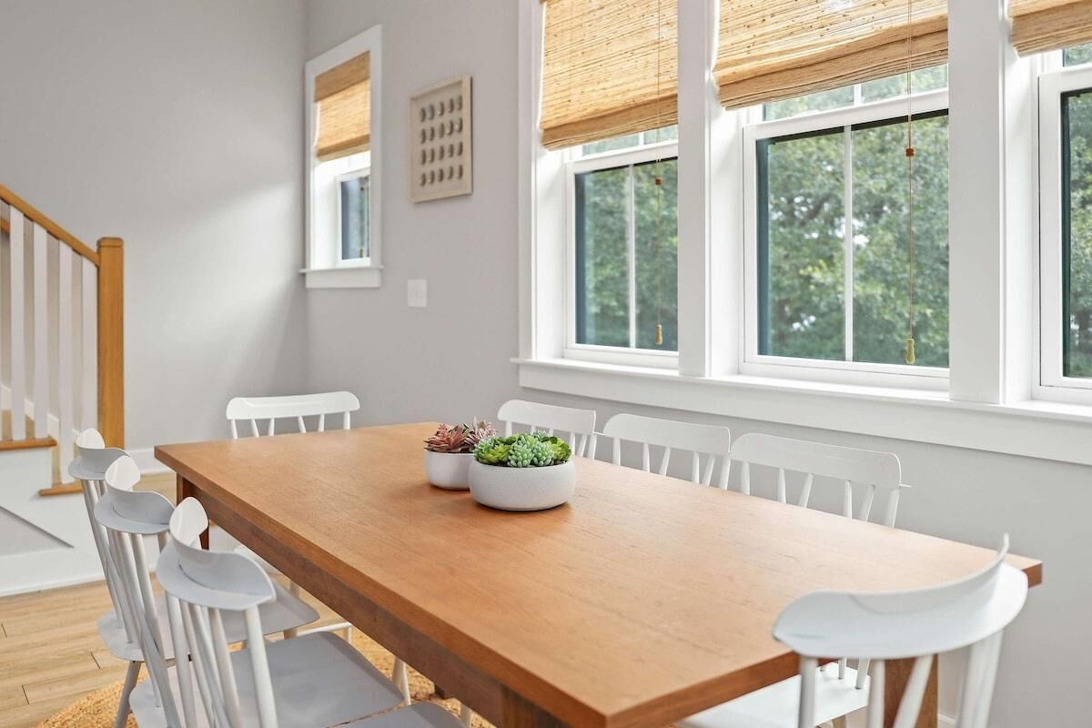 Un coin repas avec une table en bois, des chaises blanches et une fenêtre donnant sur un paysage verdoyant.