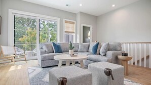 A spacious living room with a grey sectional sofa, two ottomans, a round coffee table, and a wooden chair. - Sincerely Shem- 7 min to Beach and Downtown CHS (Mount Pleasant)