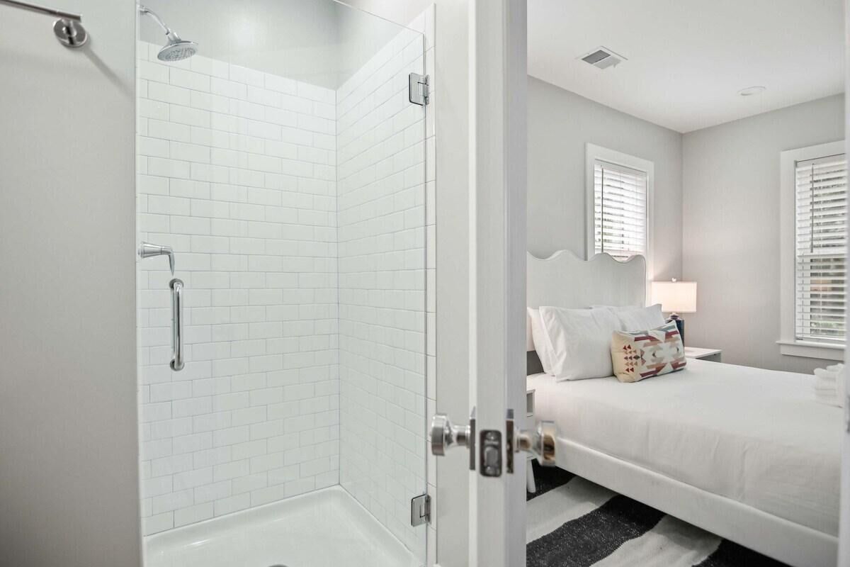 Ein modernes Badezimmer mit Duschkabine aus Glas, einer weißen Badewanne und einem Bett mit weißer Bettwäsche und Kissen.