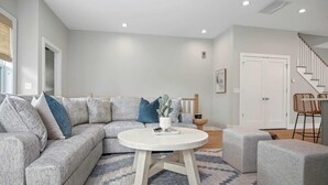 A modern living room with a gray sectional sofa, a round coffee table, and ottomans. - Sincerely Shem- 7 min to Beach and Downtown CHS (Mount Pleasant)