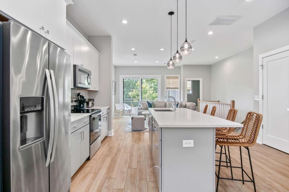 A modern kitchen with stainless steel appliances, a central island with bar stools, and a view to a balcony.