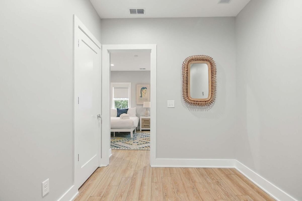 Un pasillo con una puerta blanca que da a un dormitorio con cama y mesita de noche.