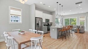 A modern kitchen with white cabinets, stainless steel appliances, and a dining area with a wooden table and white chairs. - Sincerely Shem- 7 min to Beach and Downtown CHS (Mount Pleasant)