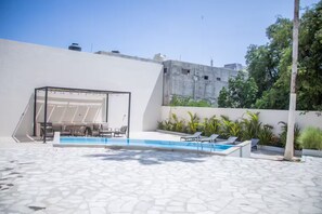 A modern outdoor pool area with a geometric pool design, a covered seating area, and surrounding greenery. - Cabo Studio 13. Three blocks away from the Marina. (Cabo San Lucas)