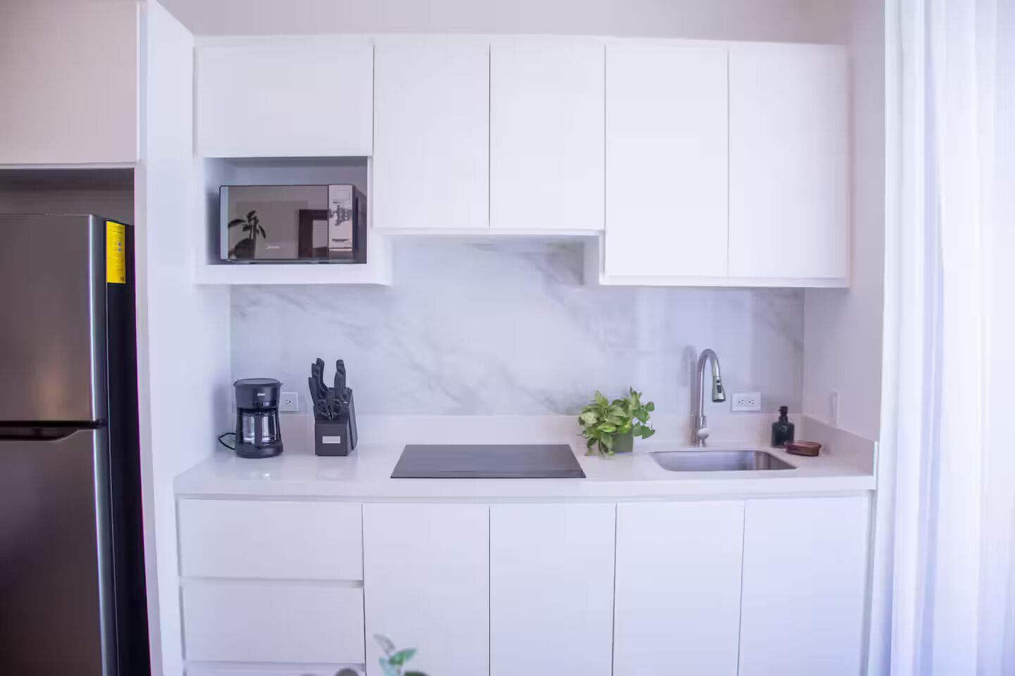 Une cuisine moderne avec des meubles blancs, un réfrigérateur en acier inoxydable, une machine à café et un évier.
