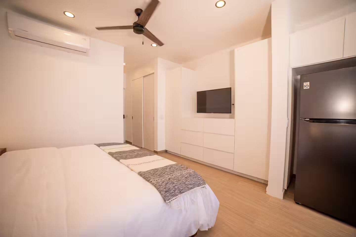 Une chambre à coucher comprenant un lit, un ventilateur de plafond, une télévision et un réfrigérateur.