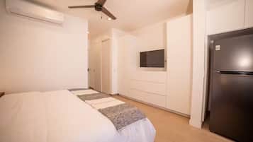 Une chambre à coucher comprenant un lit, un ventilateur de plafond, une télévision et un réfrigérateur.
