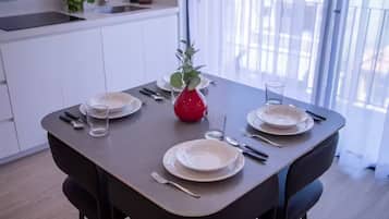 Une table à manger dressée avec des assiettes, des couverts et des verres, et un vase rouge placé au centre.