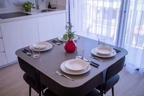 Une table à manger dressée avec des assiettes, des couverts et des verres, et un vase rouge placé au centre.