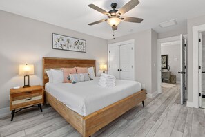 Un dormitorio con una cama de madera, dos mesitas de noche con lámparas, un ventilador de techo y una puerta que da a otra habitación.
